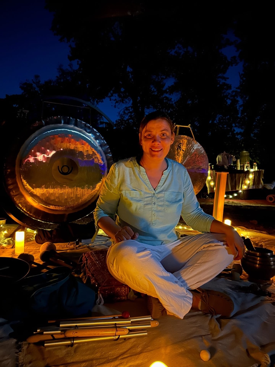 Julia Vorontsova seated outdoors with planetary gongs, candles, and instruments at dusk