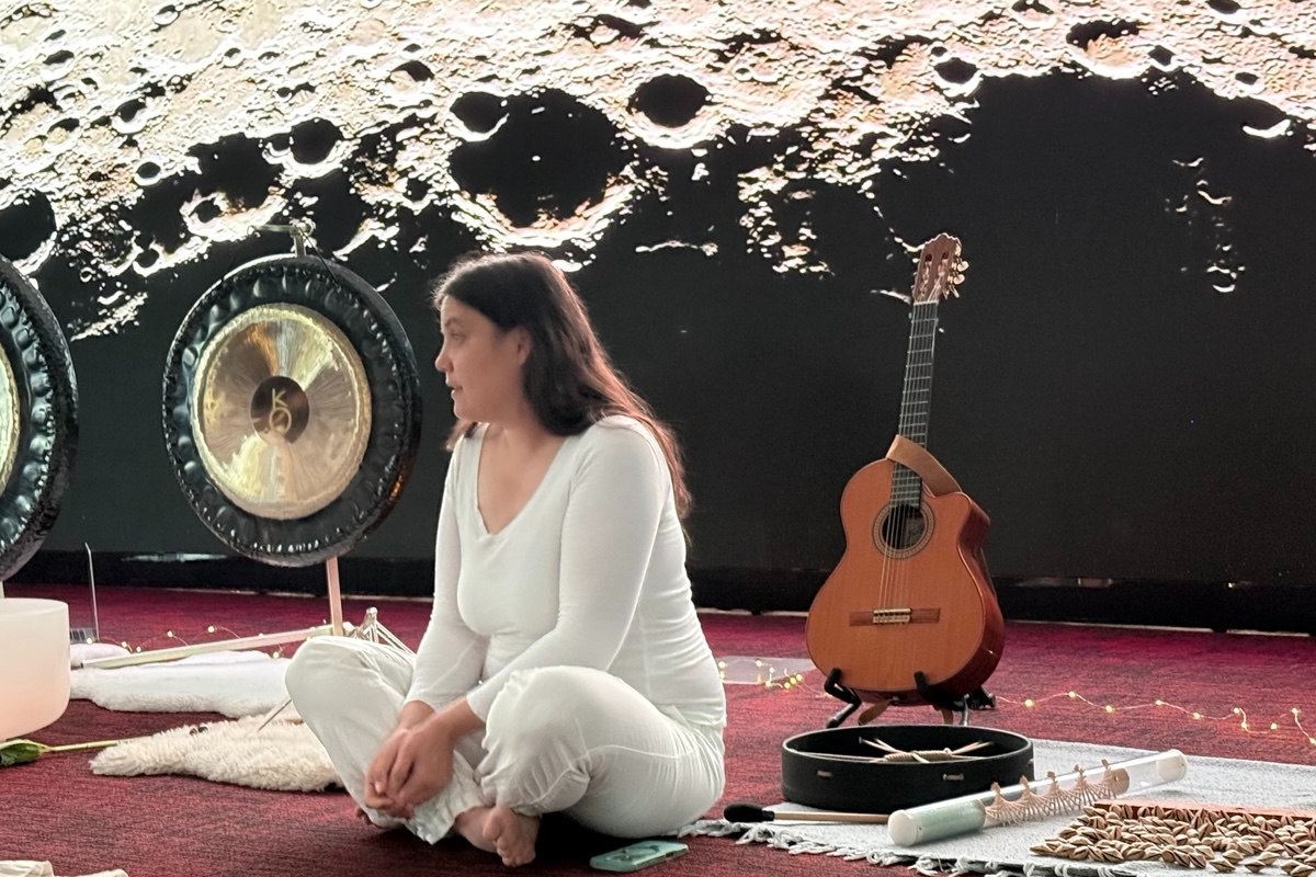Julia seated with gong, guitar, and instruments against a lunar projection